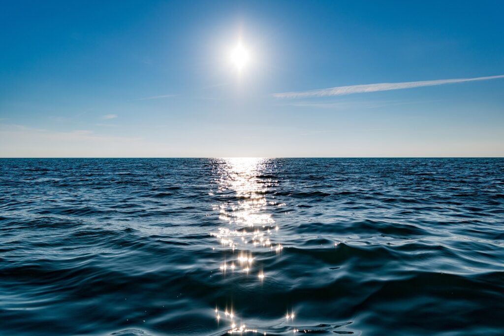 A calm ocean horizon at dusk with soft sunlight reflecting on gentle foreground waves, symbolizing a quiet mind and emotional regulation.